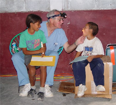 Dentist with girl on lap reaching over to look in small boys mouth