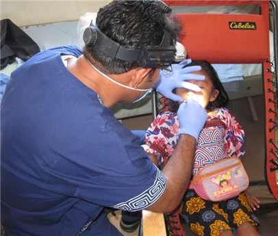 Dental volunteer examining a small child in a red chair