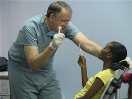 Photo of patient looking at herself in a dental mirror while a volunteer talks to her